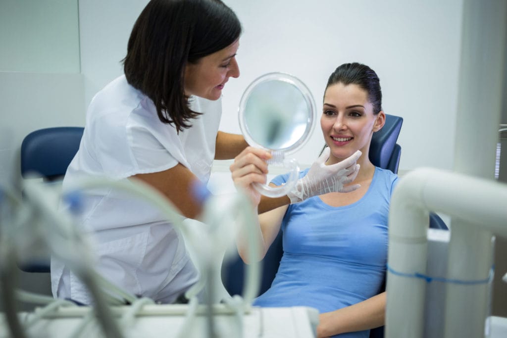 woman in blue shirt holding a mirror to her teeth