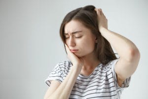 Female patient holding her cheek in visible discomfort, experiencing severe tooth or jaw pain requiring dental evaluation.