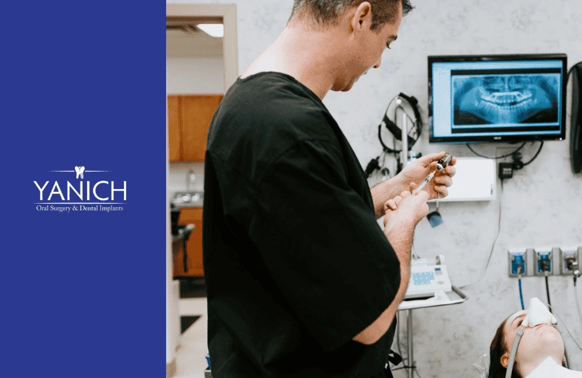 Oral surgeon preparing anesthesia in a dental operatory with advanced imaging technology displayed on a monitor.